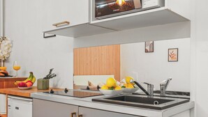 A modern kitchen with a built-in oven, a double sink, and a wooden panel wall. - Studio Champs-Élysées Arc Retreat (Paris)