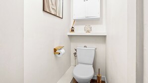 A small, white bathroom with a toilet, a roll of toilet paper, a cabinet above the toilet, and a framed picture on the wall. - Studio Champs-Élysées Arc Retreat (Paris)