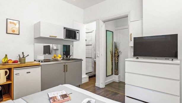 A compact hotel room with a kitchenette, a bed, a TV, and a view of the outside. - Studio Champs-Élysées Arc Retreat (Paris)