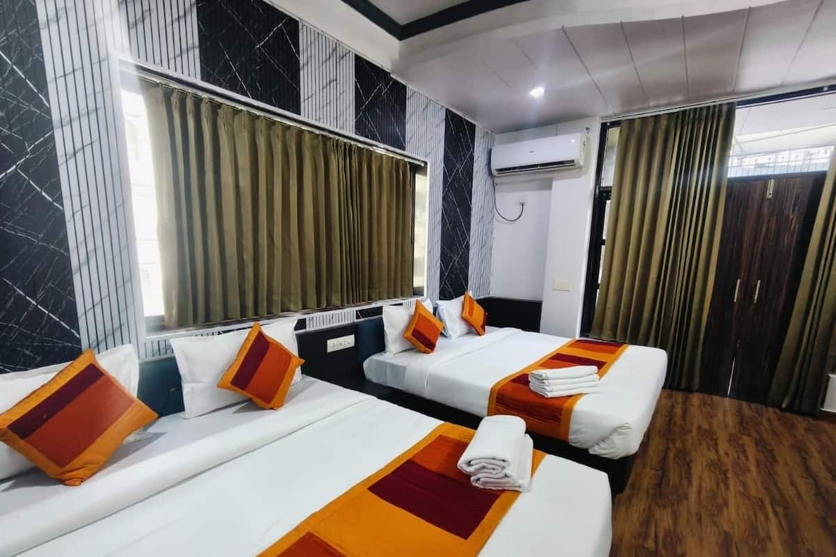 Habitación de hotel con dos camas, una ventana con cortinas, un equipo de aire acondicionado y suelo de madera.