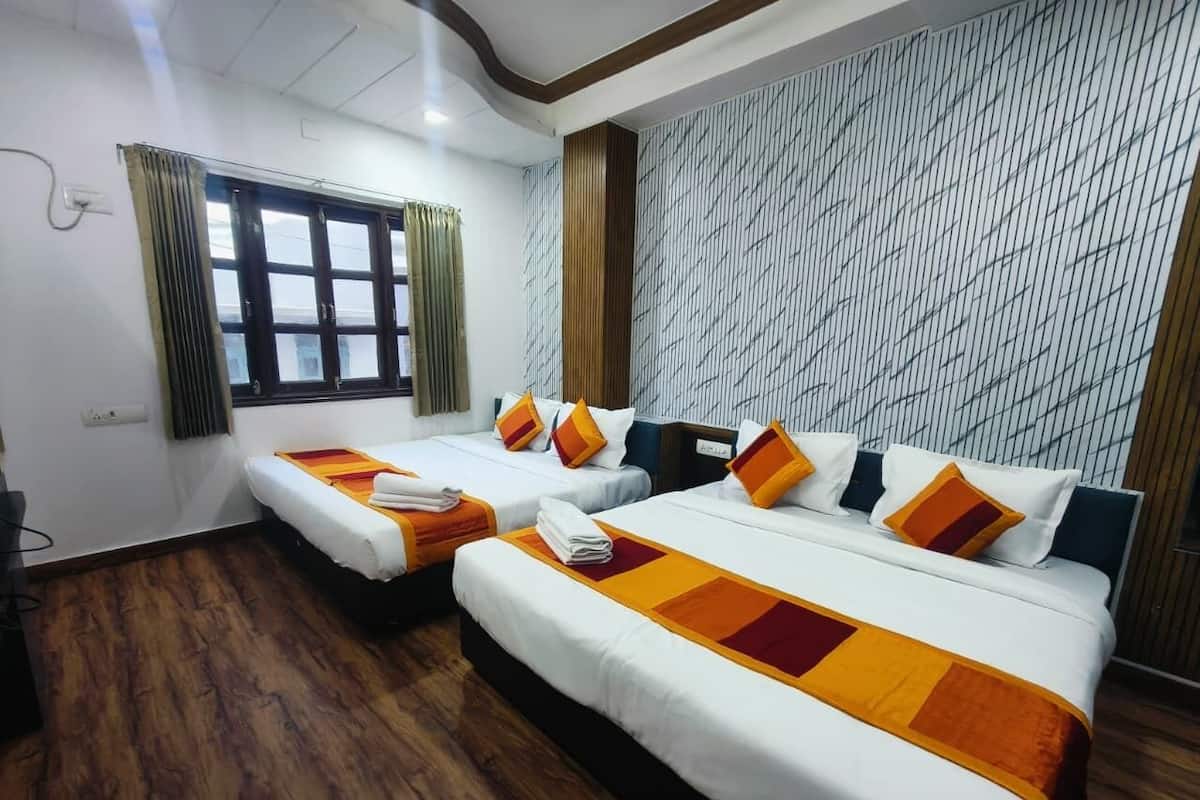 Una habitación de hotel con dos camas, una ventana con cortinas, un papel tapiz estampado y suelo de madera.