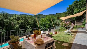 Area pranzo all'aperto con tavolo apparecchiato per due, circondata da una piscina e vegetazione.