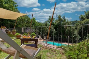 A poolside area with a table, chairs, and a shaded area. - Leccio, bright apartment with view over the valley and with swimming pool (Sassetta (LI))