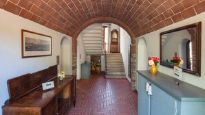 Un corridoio con soffitto in mattoni, una panca in legno, un banco receptione con uno specchio e una scala che conduce a un piano superiore.
