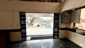 Une entrée d’immeuble avec un sol carrelé, une grille métallique et une vue sur l’extérieur.