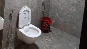 Une salle de bain avec des toilettes, une douche et un seau rouge.