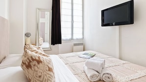 A hotel room with a bed, a TV mounted on the wall, a window with curtains, and a mirror. - 1BR Saint-Germain-des-Prés Seine Escape (Paris)