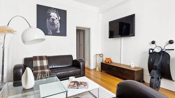 A modern living room with a leather sofa, a glass coffee table, a mounted TV, and a scooter. - 1BR Saint-Germain-des-Prés Seine Escape (Paris)