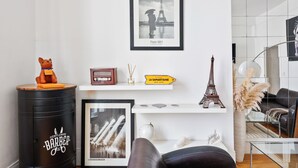A modern living room with a framed Paris 1951 photograph, a small Eiffel Tower model, a vintage radio, and a directional sign. - 1BR Saint-Germain-des-Prés Seine Escape (Paris)