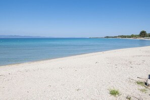 Ein Strand mit klarem Wasser, einem sandigen Ufer und Bergen im Hintergrund.