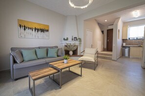Ein modernes Wohnzimmer mit einer Couch, einem Couchtisch und einem Sessel, im Hintergrund eine Küche und eine Treppe, die in eine weitere Ebene führt.