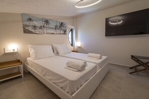 Ein Doppelbett mit weißen Leinen, ein Nachttisch, ein an der Wand befestigtes Fernsehgerät und ein Palmen-Gemälde.