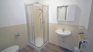 Et badeværelse med en glasafskærmet brusekabine, en håndvask og et toilet.