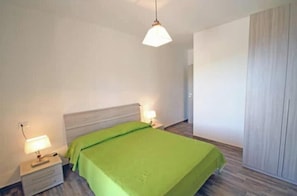 Ein Schlafzimmer mit einem Bett, Nachttischlampen, einem Beistelltisch und einer Pendelleuchte.