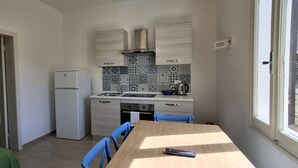Ett kompakt kök med kylskåp, spis och diskho, ett matbord med stolar och ett fönster som släpper in naturligt ljus.