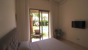 Une chambre avec un lit, un téléviseur fixé au mur et une vue sur une piscine et un espace de détente extérieur, accessible par une porte coulissante.