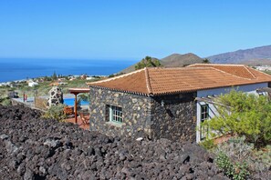 A stone building with a tiled roof, a pool, and a view of the ocean. - Independent holiday home in La Palma with a community pool (Los Llanos de Aridane)