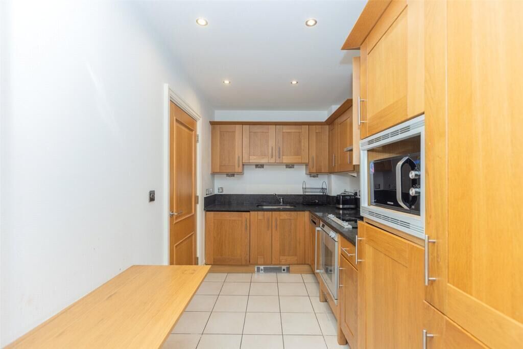 A compact kitchen with wooden cabinets, a black countertop, and a built-in oven.
