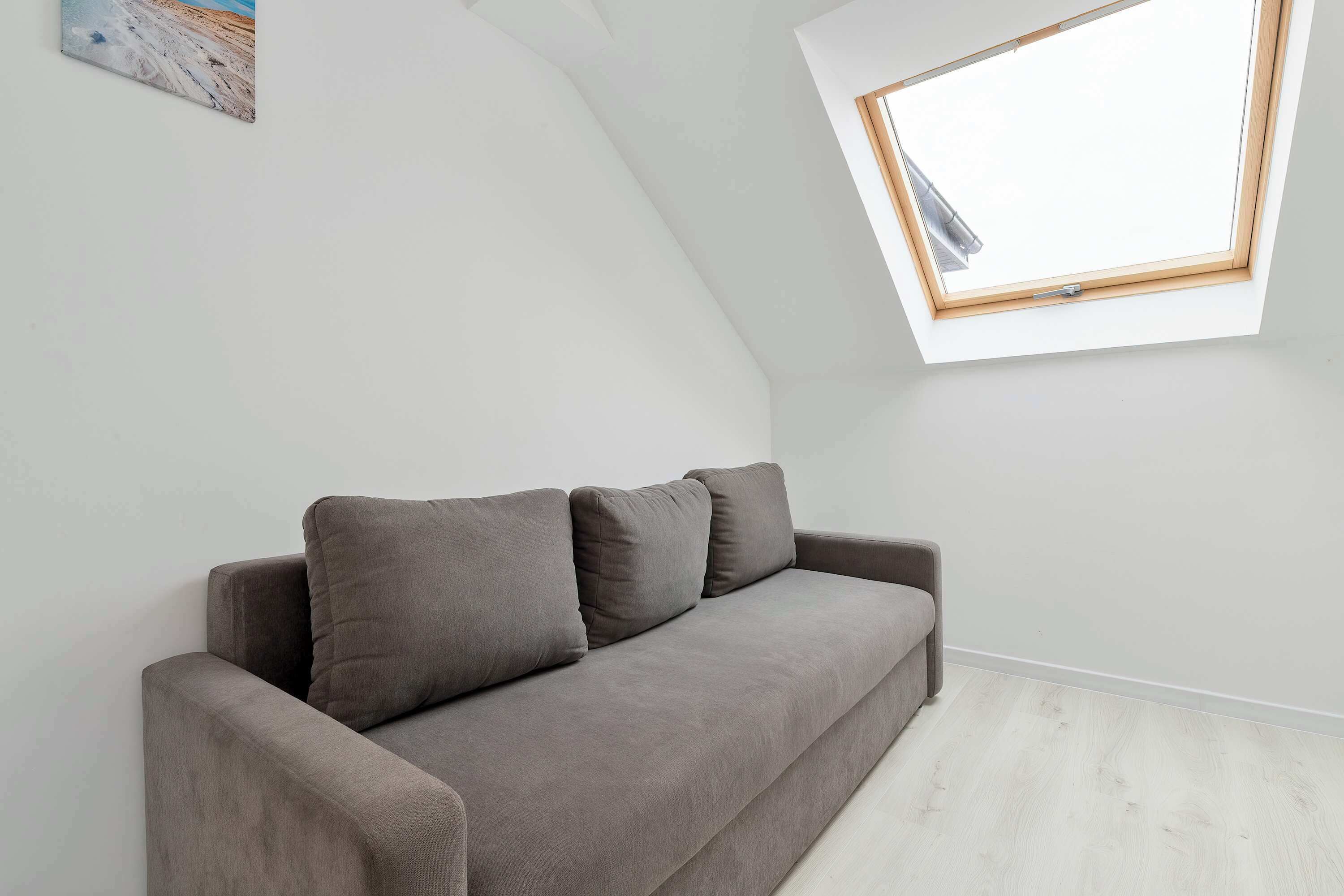 A grey sofa with cushions in a room with a sloped ceiling and a skylight.