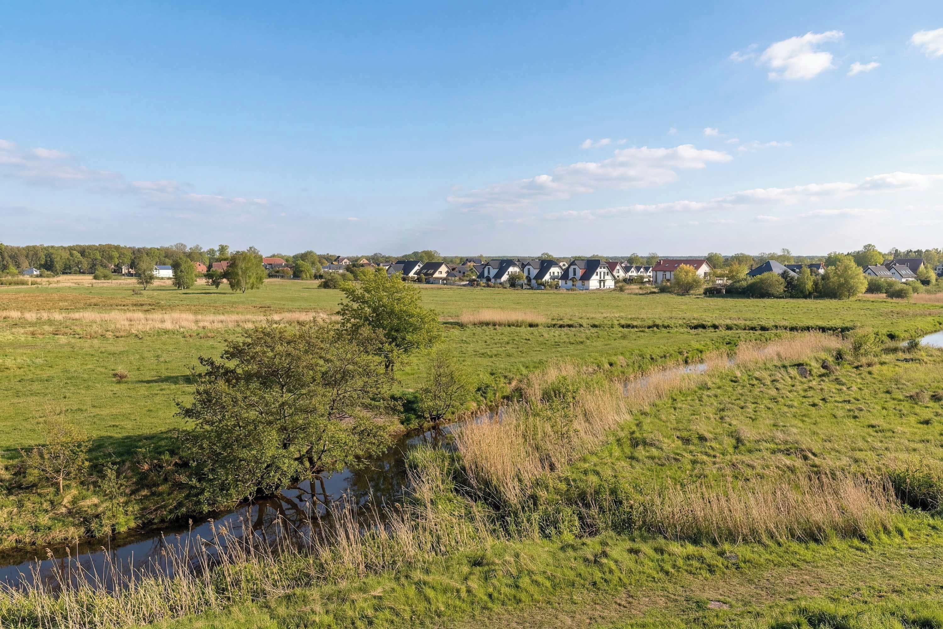Ländliche Landschaft mit einer Reihe von Häusern, einem Bach und offenen Feldern.
