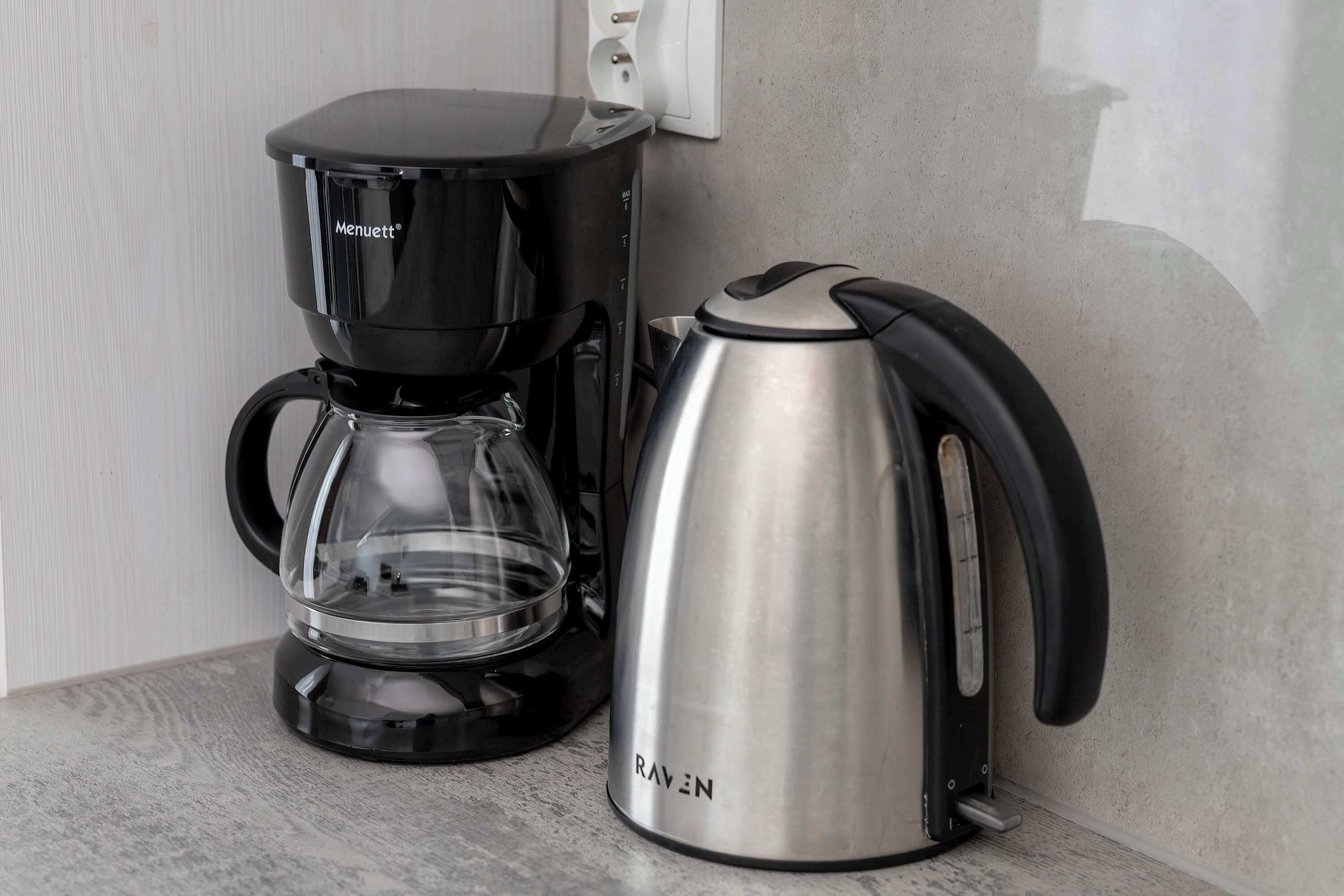 Una cafetera negra y un hervidor de acero inoxidable sobre una encimera de cocina.