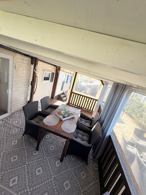 A covered patio area with a table set for two, surrounded by wicker furniture.