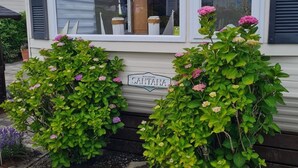 A mobile home with a window, two potted plants with flowers, and a sign that reads 'SANTA ANA.'