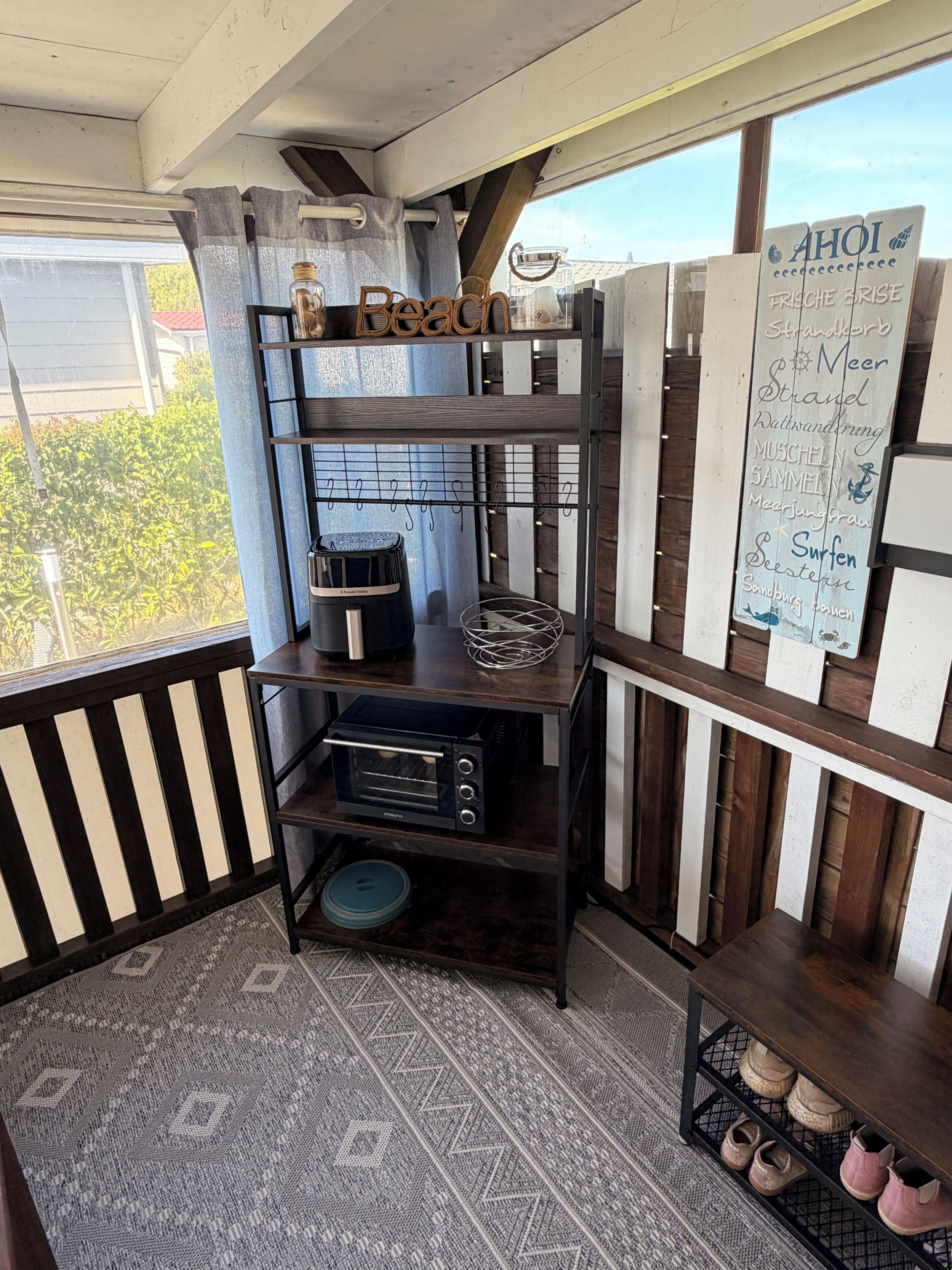A corner of a room with a dark wooden shelf unit, a black toaster oven, a small table with a glass container, and a sign listing various destinations.