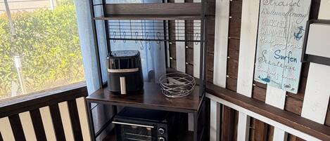 A corner of a room with a dark wooden shelf unit, a black toaster oven, a small table with a glass container, and a sign listing various destinations.