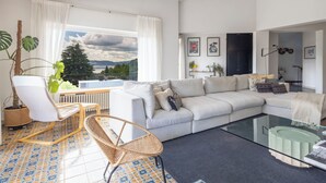 Una sala moderna con un sofá, una mesa de centro de vidrio, un sillón de mimbre y vistas a un lago a través de amplios ventanales.
