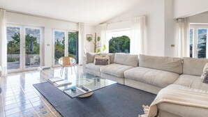 Una sala de estar con sofá, una mesa de centro de cristal y vistas al exterior a través de grandes puertas correderas.