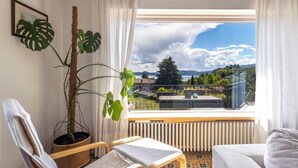 Una habitación con vistas a un lago, una planta en maceta, una silla, un sofá y un radiador.