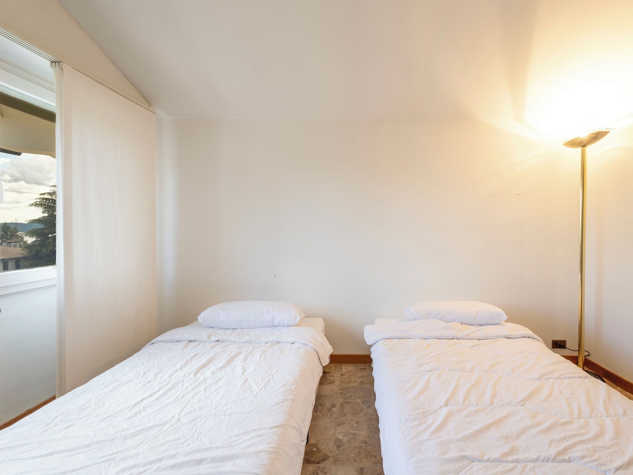 Een kleine, schone kamer met twee eenpersoonsbedden, een raam met uitzicht en een vloerlamp.