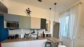 A compact kitchen with a sink, a coffee maker, a toaster, and a small refrigerator. There is a wooden dining table with two stools. - Cannes Port | Suite 4 | 2 min Palais (Cannes)