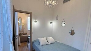 A bedroom with a bed, a chandelier, a mirror, and a door leading to another room. - Cannes Port | Suite 4 | 2 min Palais (Cannes)