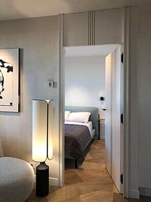 A hotel room with a bed, bedside table, lamp, and a painting on the wall. - Cannes Port | Suite 2 | Vue imprenable Palais (Cannes)