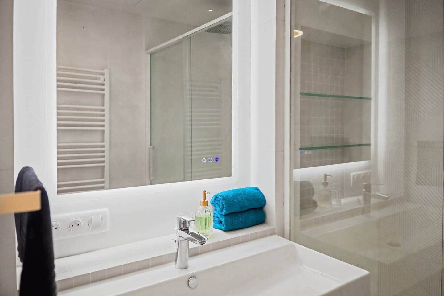 Une salle de bain avec un lavabo blanc, un miroir, une cabine de douche en verre et un porte-serviettes.