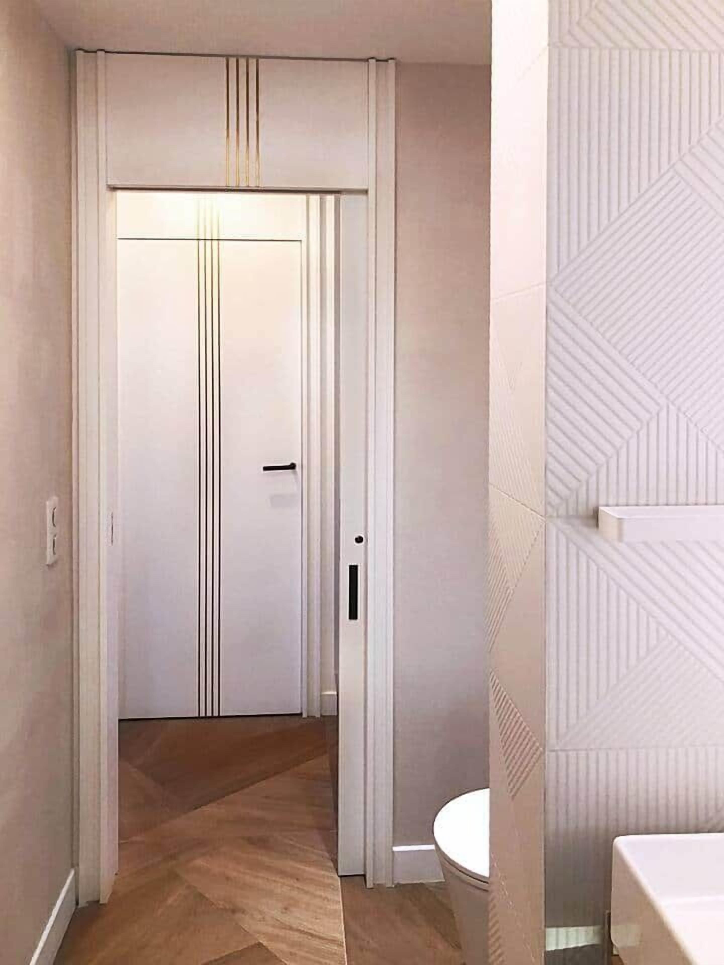 Un pasillo que lleva a una puerta con picaporte, un inodoro y un papel tapiz estampado.