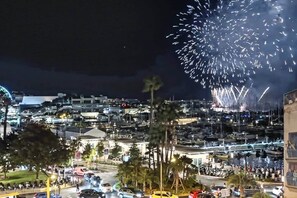 A nighttime cityscape with fireworks, a marina, and a road with vehicles and pedestrians. - Cannes Port | Suite 2 | Vue imprenable Palais (Cannes)
