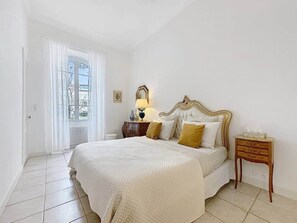 Ein Schlafzimmer mit einem Bett, Nachttischen, einer Lampe und einem Fenster mit Vorhängen.