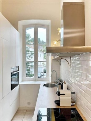 Una cocina moderna con ventana, armarios blancos, un lavamanos de acero inoxidable y una estufa negra.