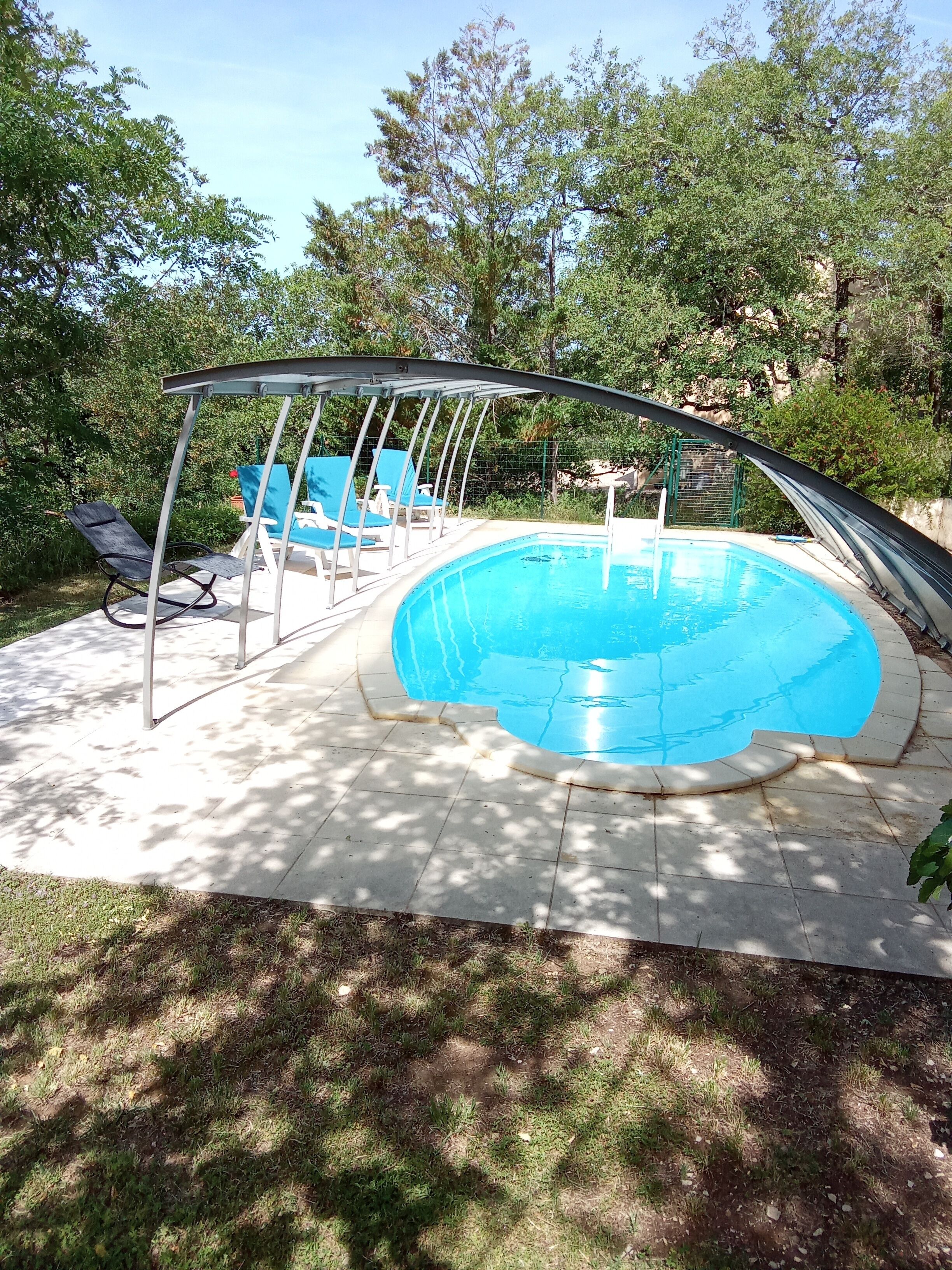 Una piscina con borde curvo, rodeada por una zona de estar techada con sillas azules.