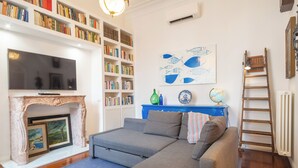 Ein Wohnzimmer mit Kamin, Bücherregalen, einer Couch, einem Fernseher und einer Leiter.