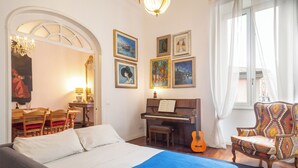 Ein Schlafzimmer mit einem Bett, einem Klavier, einer Gitarre, einem Sessel und Bildern an den Wänden.