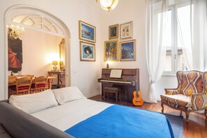 Ein Schlafzimmer mit einem Bett, einem Klavier, einer Gitarre, einem Sessel und Bildern an den Wänden.