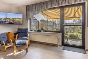 Una sala de estar con televisor, radiador, ventana y vista a barcos, además de una silla.