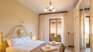 Une chambre d’hôtel avec un lit, des tables de chevet, un lustre, une porte-fenêtre donnant sur un balcon et une vue sur l’extérieur.