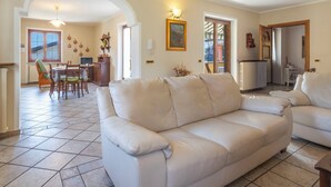 Un salon comprenant un canapé, une table à manger, des chaises et un coin cuisine visible à travers une porte ouverte.
