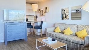 Ett modernt vardagsrum med en soffa, ett soffbord, en tv och ett köksområde.
