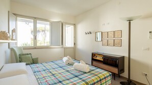 Ein Schlafzimmer mit einem Bett, einem Schminktisch, einer Lampe und einem Fenster mit geöffneter Tür.